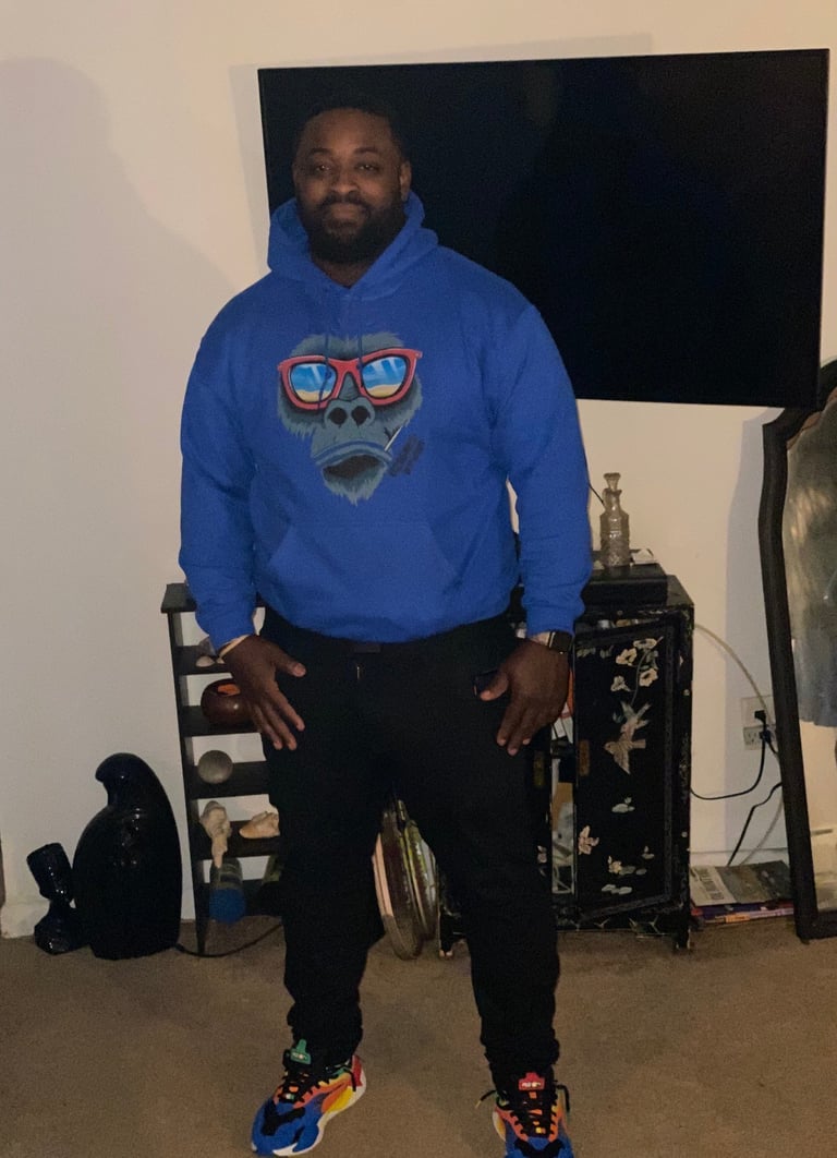 Man in blue hoodie with graphic design standing in living room with furniture and TV in background