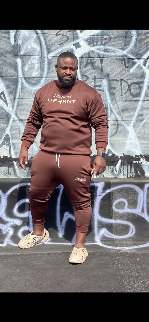 Man in burgundy Designed tracksuit posing in front of graffiti wall wearing cream sneakers