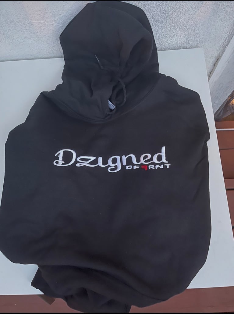 Black hoodie with Designed Different white text logo displayed on indoor shelf