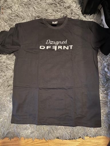 Black t-shirt with Designed DEFIANT text printed on chest, laid flat on gray textured fabric