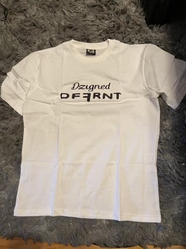 White t-shirt with black text reading Designed DEFIANT laid on a gray textured surface