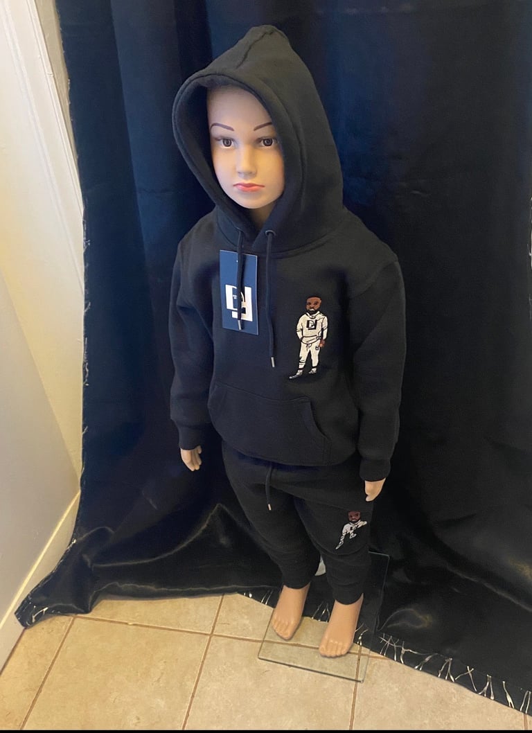 Mannequin wearing black hoodie with graphic design and matching black pants against blue curtain backdrop