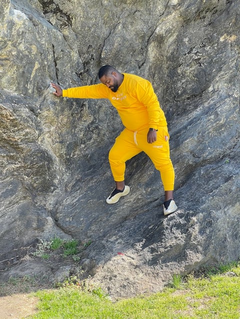 Man in yellow athletic outfit rock climbing on a large gray stone wall outdoors